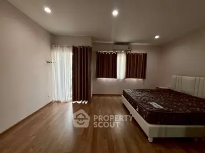 Spacious bedroom with wooden flooring and large windows for natural light