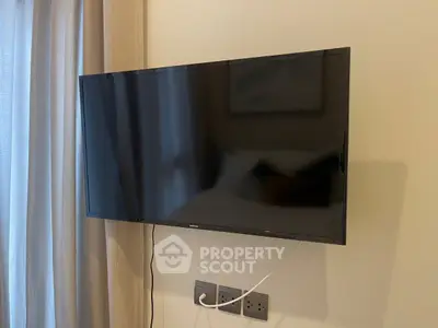 Modern wall-mounted TV in a stylish living room with neutral tones and elegant curtains.