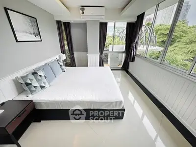 Spacious bedroom with large windows and modern decor, offering a serene view of greenery.