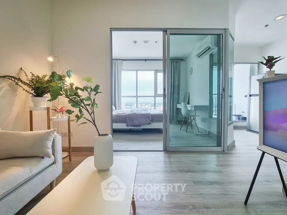 Modern open-plan living room with a view into a cozy bedroom, featuring stylish decor and natural light.