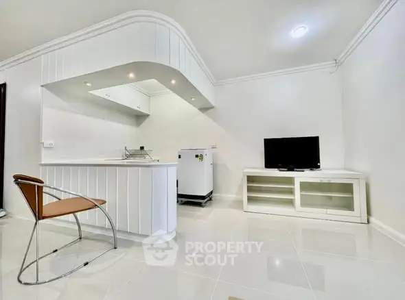 Modern minimalist living room with sleek white furniture and open kitchen layout.