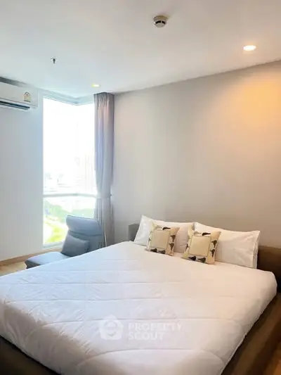 Spacious bedroom with large window offering city views, modern furnishings, and cozy ambiance.