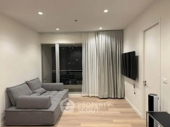 Modern living room with sleek gray sofa and wall-mounted TV, featuring elegant curtains and wooden flooring.