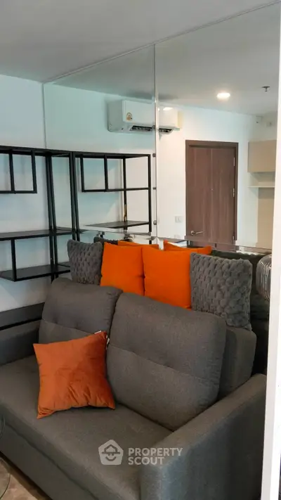 Modern living room with stylish gray sofa and vibrant orange cushions, featuring sleek shelving and a mirrored wall.