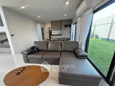Modern living room with sleek sofa and garden view, open layout to kitchen area.