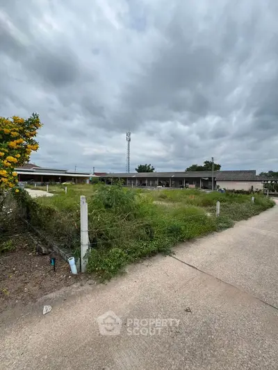 Expansive plot of land with potential for development under a cloudy sky, featuring lush greenery and a paved pathway.