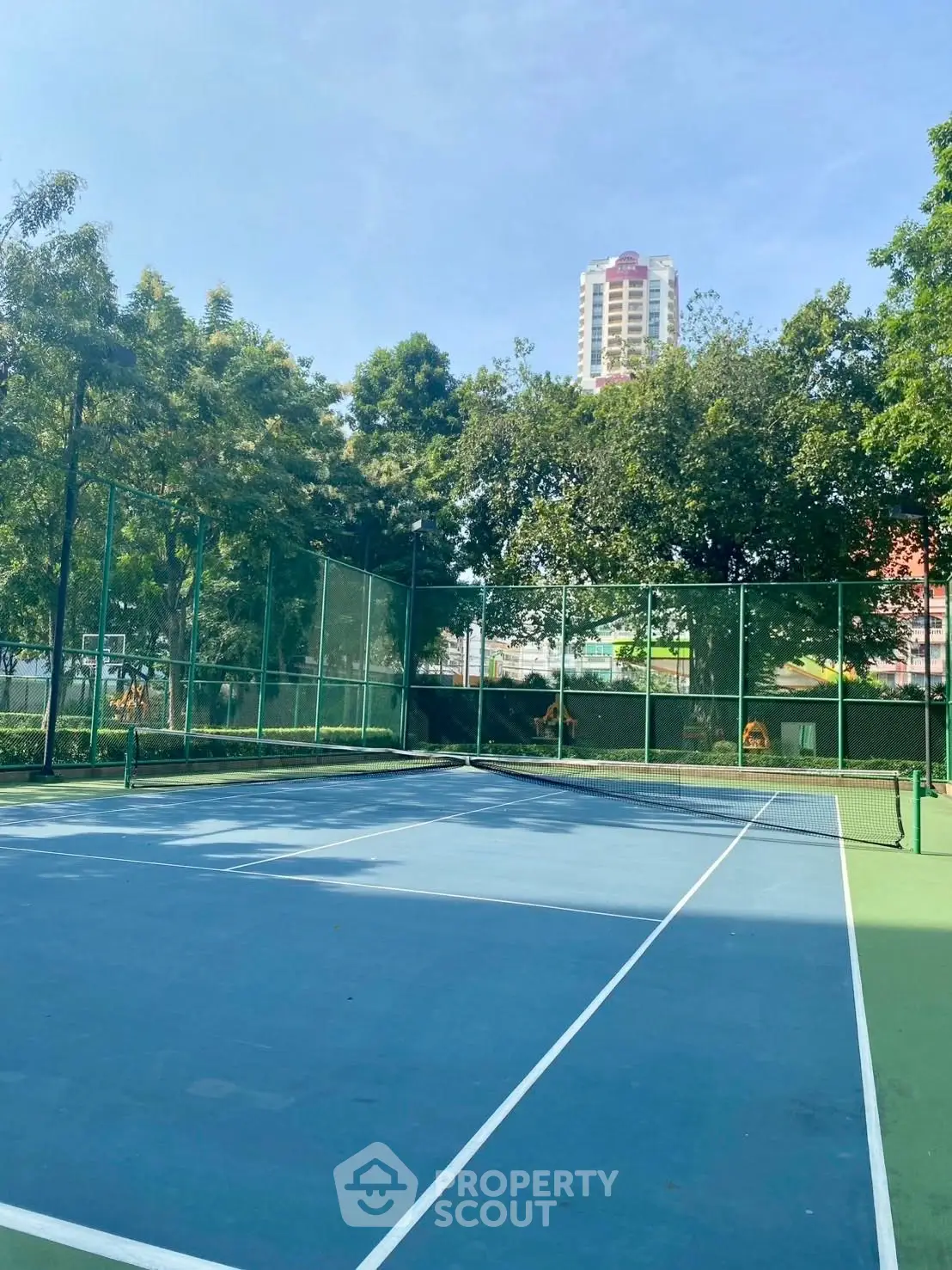 Spacious outdoor tennis court with lush greenery and city skyline view, perfect for sports enthusiasts.