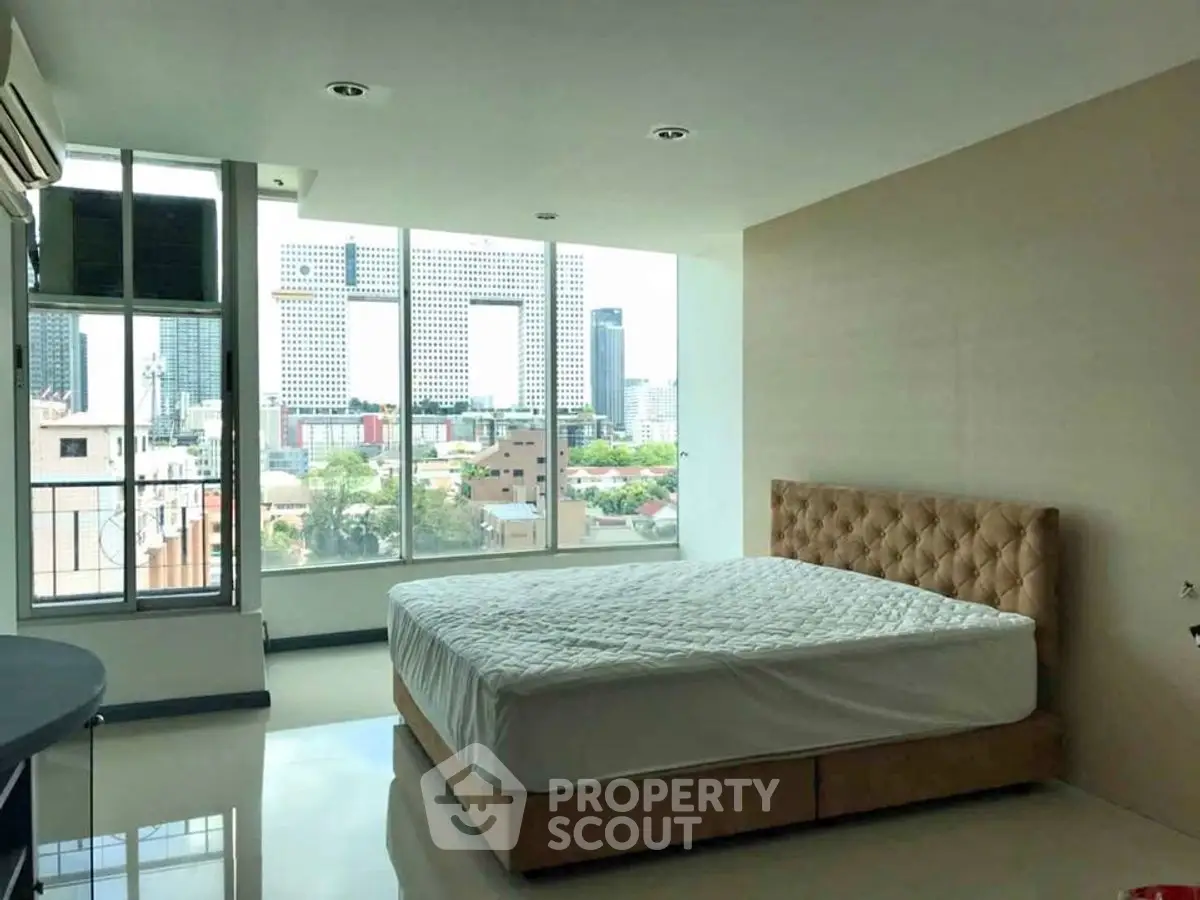 Spacious bedroom with large windows offering a stunning city view, featuring a plush bed and modern decor.