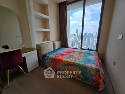 Modern bedroom with vibrant bedspread and stunning city view from large window.