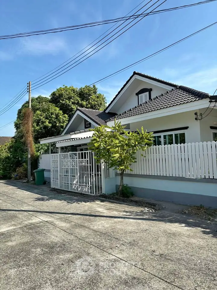 Charming suburban house with white picket fence and lush greenery under clear blue sky.