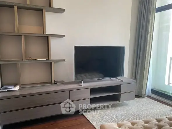 Modern living room with sleek TV stand and large flat-screen TV, featuring elegant shelving and floor-to-ceiling window.