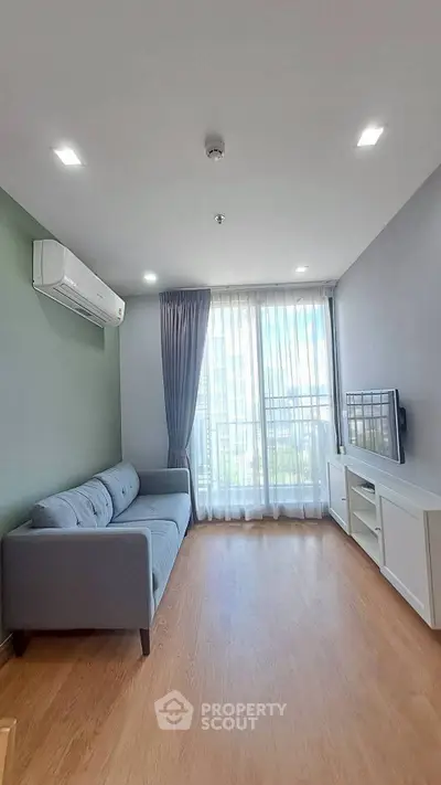 Modern living room with large window, stylish sofa, and sleek TV setup in a bright apartment.
