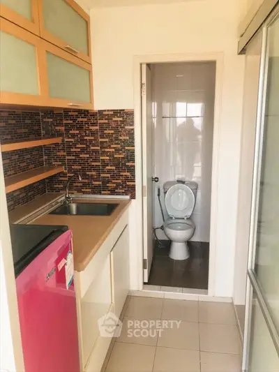 Compact kitchen with modern backsplash and adjacent bathroom in cozy apartment.