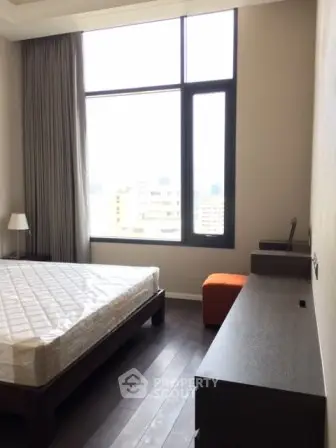 Modern bedroom with large window and stylish furniture in urban apartment.
