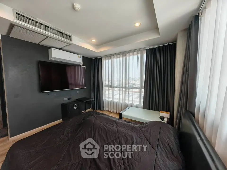 Modern bedroom with large windows and city view, featuring a sleek TV and stylish decor.