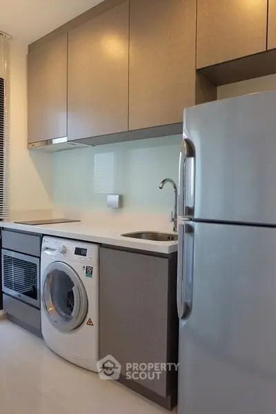 Modern kitchen with sleek cabinets, washing machine, and stainless steel fridge in a compact layout.