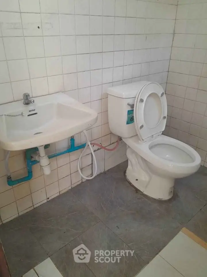 Simple bathroom with white tiles, sink, and toilet in a real estate property.