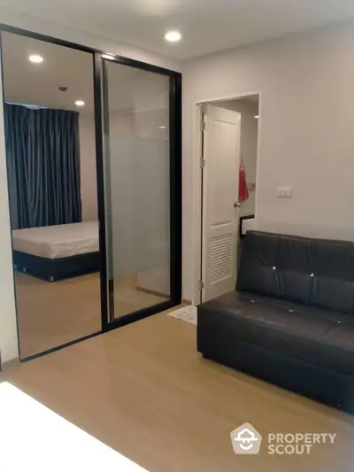 Modern studio apartment with sleek furniture and large mirror wardrobe, offering a cozy living space with a comfortable sofa and a glimpse of the bedroom area.