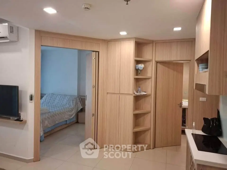 Modern apartment interior with open kitchen and cozy bedroom view, featuring sleek wooden cabinetry and contemporary design.
