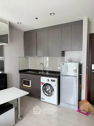 Modern kitchen with sleek cabinets, washing machine, and compact fridge in a stylish apartment.