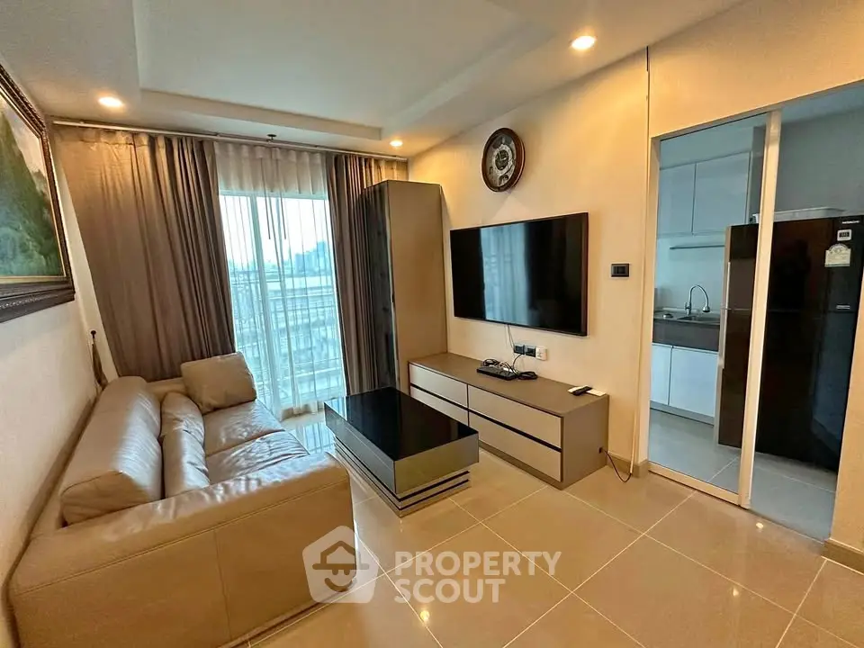 Modern living room with sleek furniture and large TV, adjacent to a stylish kitchen.