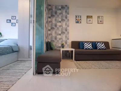 Modern living room with stylish decor and cozy seating area, adjacent to a bedroom with sliding glass doors.
