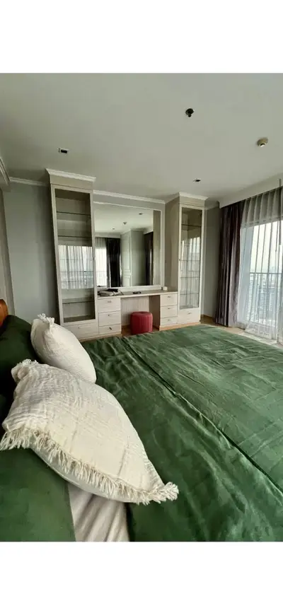 Spacious bedroom with green bedding and large windows offering natural light and balcony access.