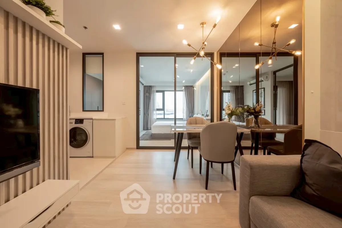 Modern open-plan living room with dining area and washing machine, featuring elegant lighting and mirrored wall.