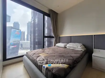 Modern bedroom with city view, featuring a cozy bed and large windows for natural light.