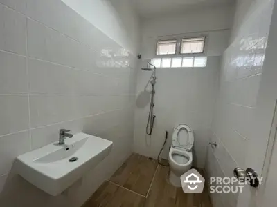 Pristine white-tiled bathroom featuring modern fixtures, a wall-mounted sink, and a spacious shower area, illuminated by natural light from frosted glass windows.