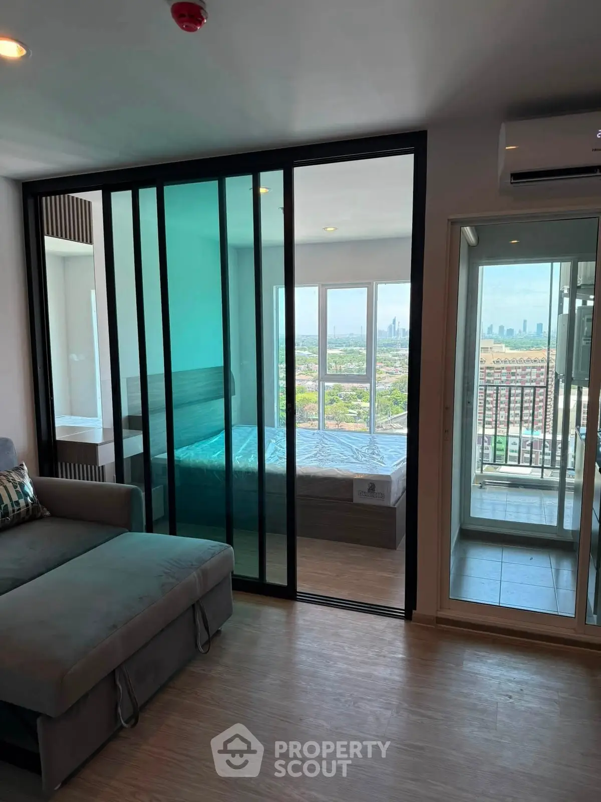 Modern apartment with glass partition, cozy living area, and stunning city view from the balcony.