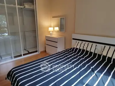 Cozy bedroom with striped bedding and mirrored wardrobe in modern apartment.
