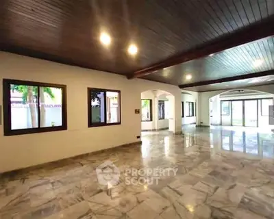 Spacious open-concept living area with marble flooring and wooden ceiling beams.