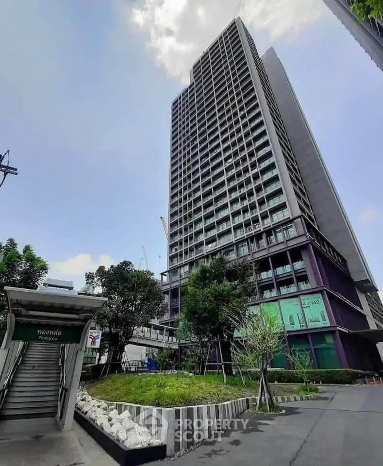 Modern high-rise building with lush green landscaping and clear blue sky.