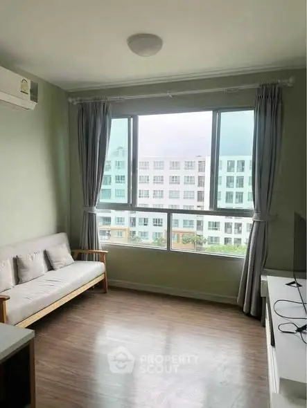 Bright living room with large window and modern furnishings in a high-rise apartment.
