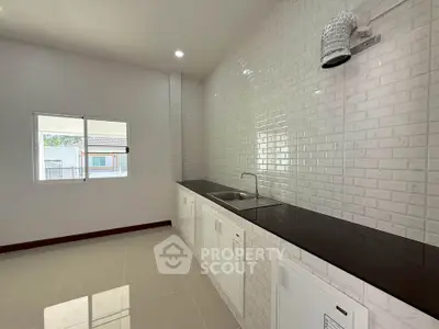 Modern kitchen with sleek white cabinetry and glossy tiled walls, featuring a large window for natural light.