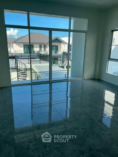 Spacious room with large windows offering a view of modern houses and a balcony.