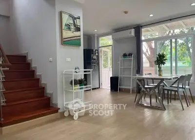 Spacious modern living area with dining set and staircase, featuring large windows and stylish decor.