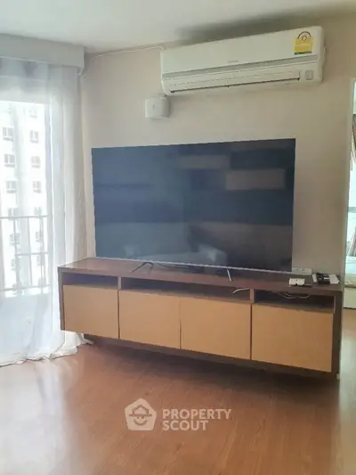 Modern living room with large TV and air conditioning, featuring wooden flooring and natural light.