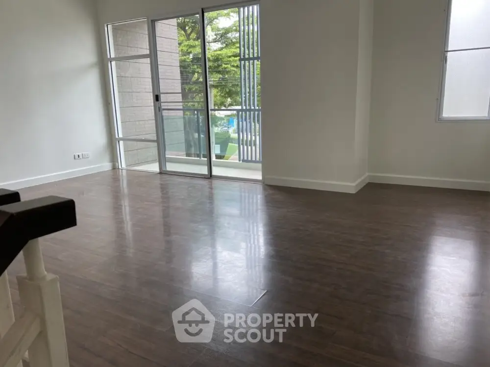 Spacious living room with wooden flooring and large windows overlooking greenery.