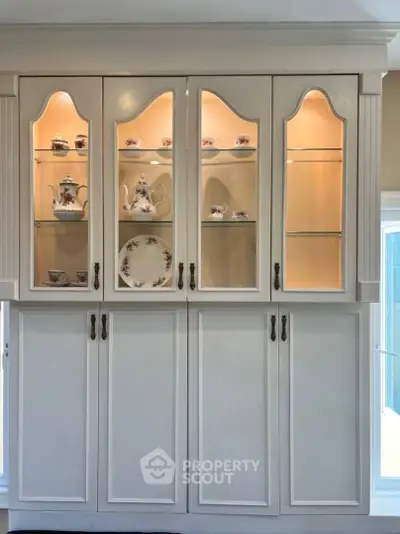 Elegant kitchen cabinet with glass doors showcasing fine china in a bright, modern kitchen.