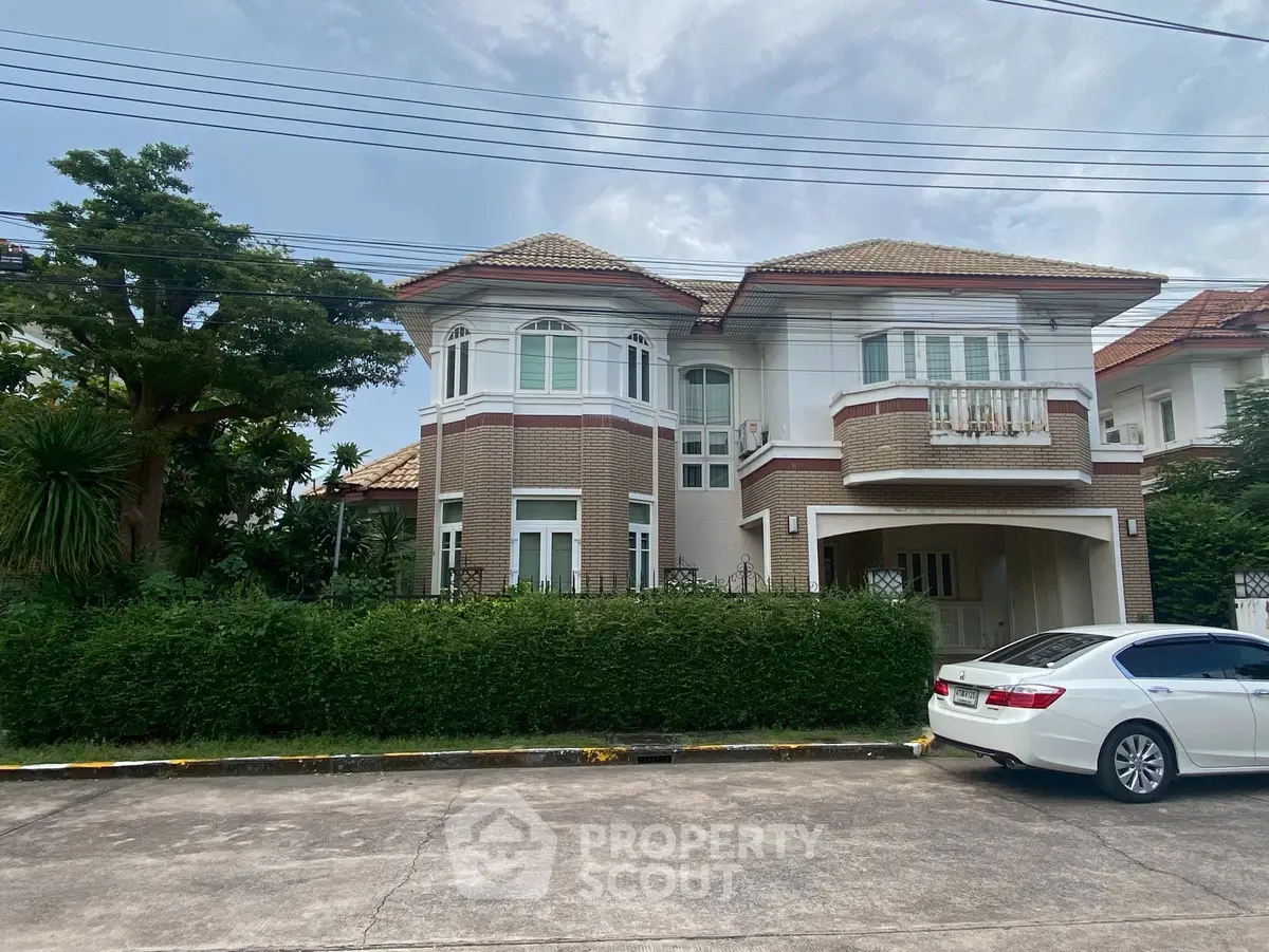 Elegant two-story house with lush greenery and a parked car in a serene neighborhood.