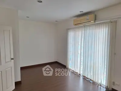 Spacious empty room with wooden flooring and large window with vertical blinds.