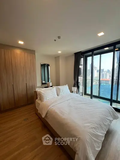 Modern bedroom with city view and large windows, featuring a cozy bed and wooden wardrobe.