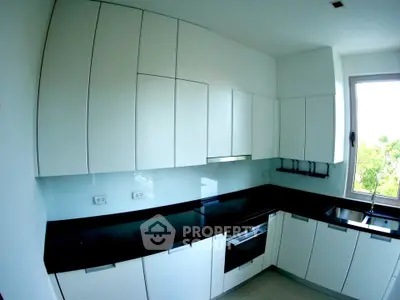 Modern kitchen with sleek white cabinets and black countertops, featuring a large window with a view.