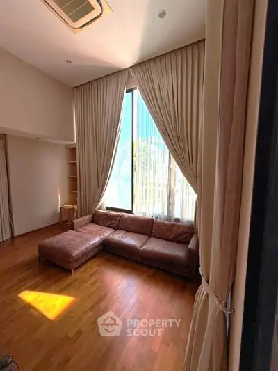 Spacious living room with high ceilings and elegant curtains, featuring a cozy leather sofa.