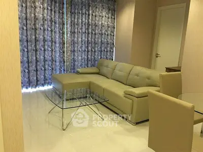 Modern living room with beige leather sofa and glass coffee table, elegant curtains and bright flooring.