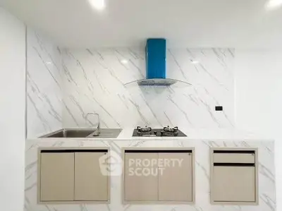 Modern kitchen with marble backsplash and gas stove, featuring sleek cabinetry and stainless steel sink.