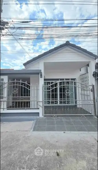 Charming single-story house with gated entrance and tiled driveway under a blue sky.