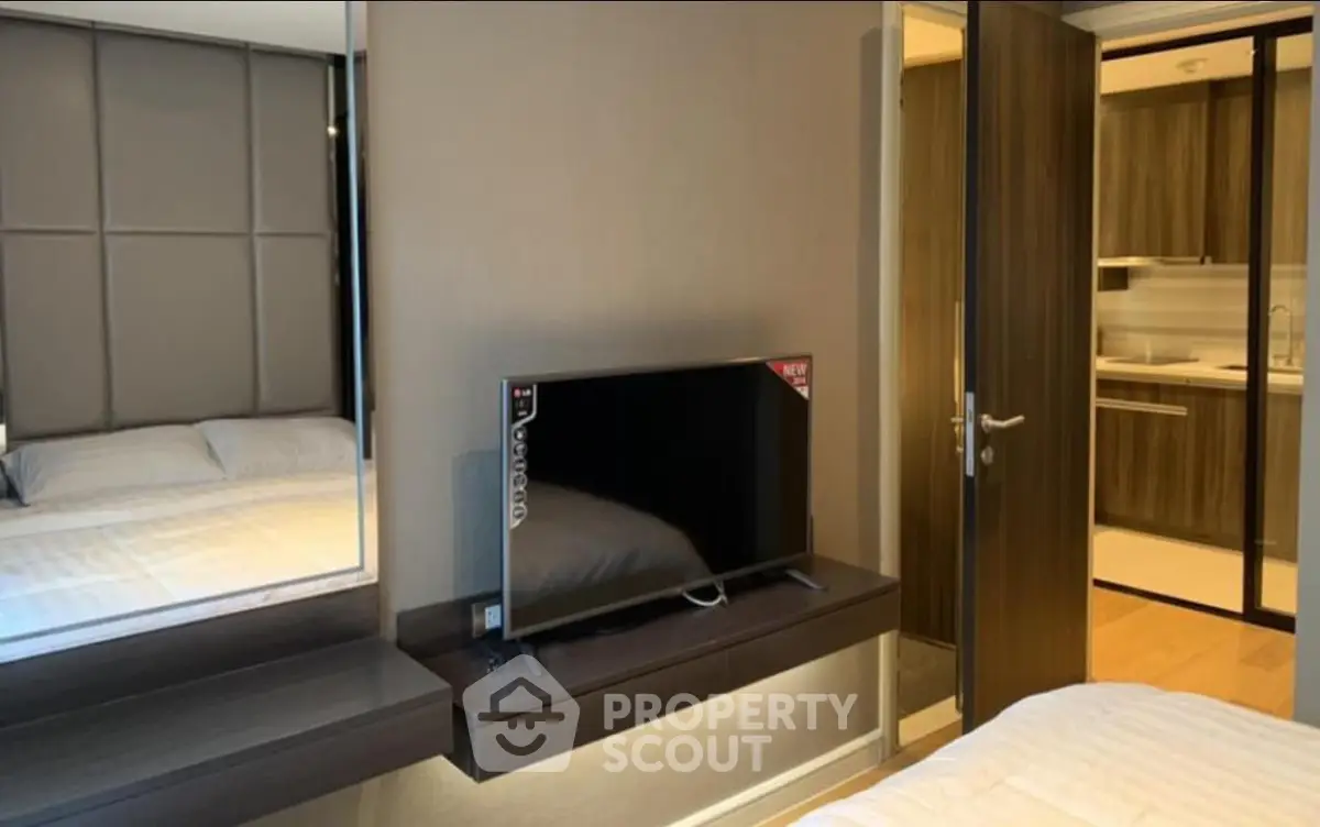 Modern bedroom with TV and view into sleek kitchen area